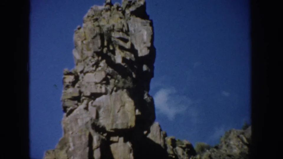 Colorado 1959 8mm frame with the rock tower shifted in view, showing cracked stone faces and a small cloud behind it.