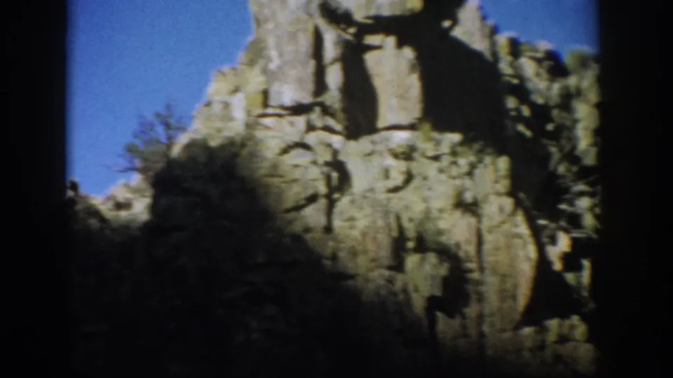 Colorado 1959 frame showing a sunlit eroded cliff and pillar, with brush at the base and dark film borders from the 8mm scan.