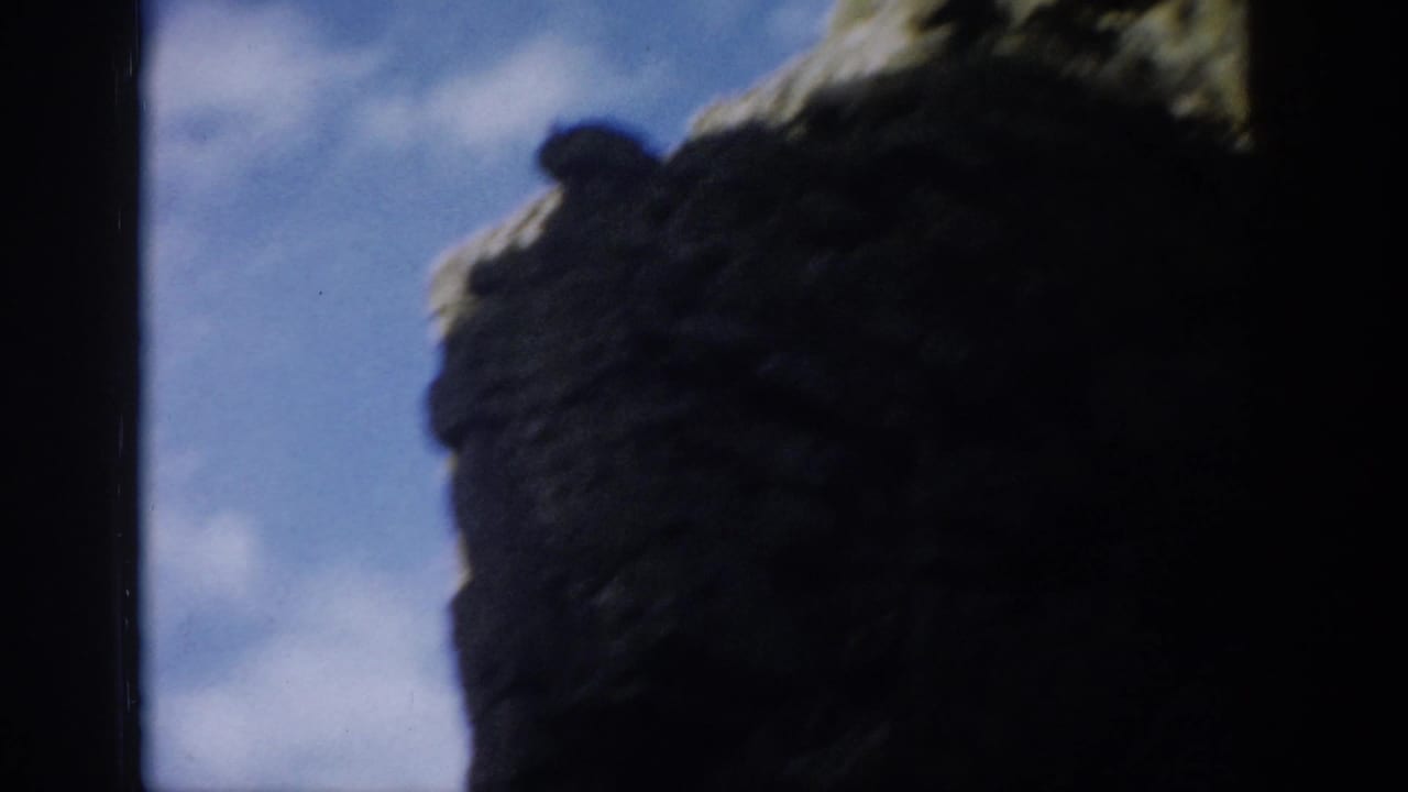 Colorado 1959 8mm frame with dark rock walls silhouetted against blue sky and a rugged mountain slope.