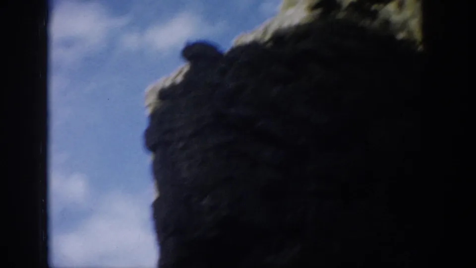 Colorado 1959 8mm frame with dark rock walls silhouetted against blue sky and a rugged mountain slope.