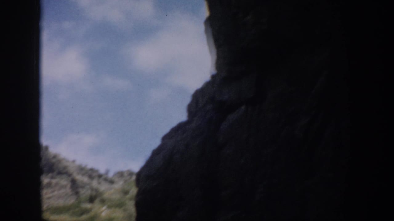 Colorado 1959 8mm view from within a shadowed rock passage toward a bright rocky mountain slope.