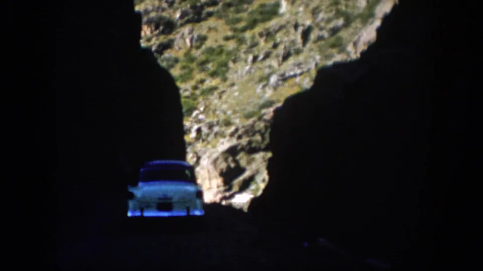 Colorado 1959 8mm frame showing a light-colored vintage car moving through a dark rock passage toward daylight.