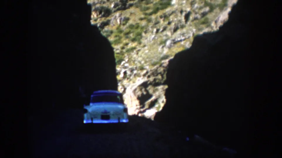 Colorado 1959 8mm frame with a pale vintage car in deep cave shadow below a sunlit rocky slope.
