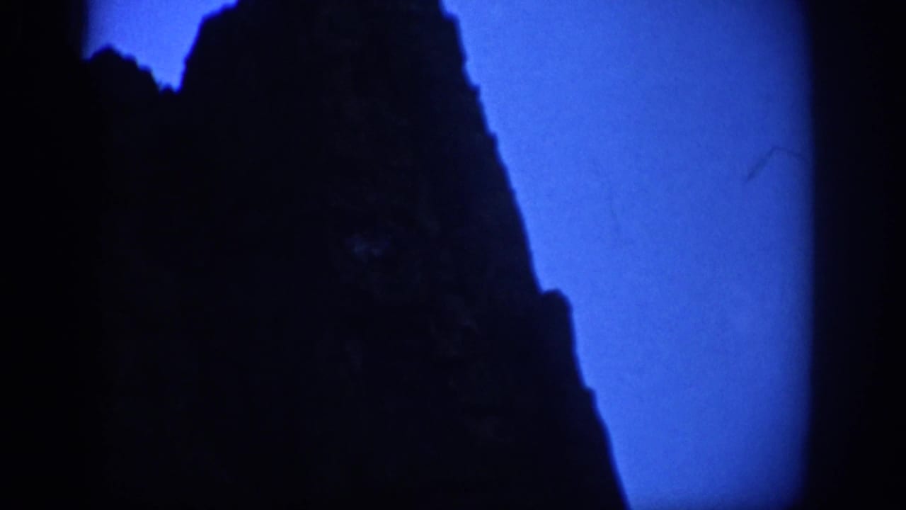 1959 Colorado 8mm frame showing a dark mountainside silhouette against a saturated blue twilight sky.