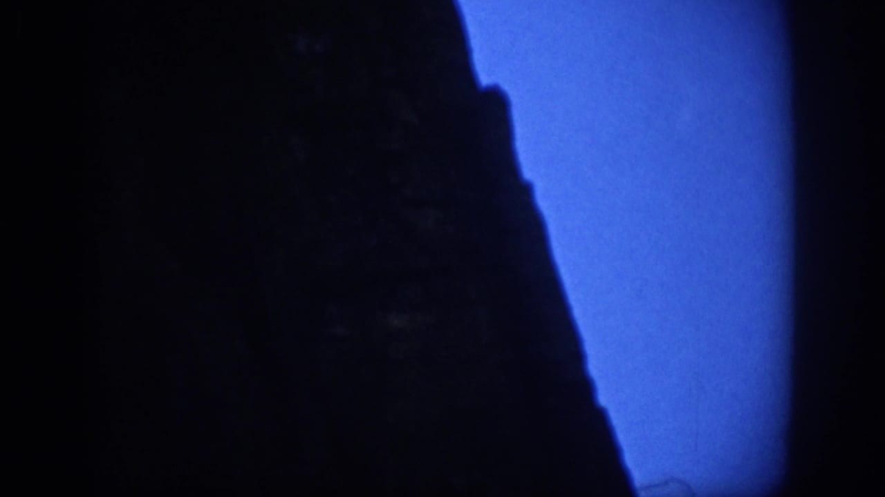 Large dark rock face fills the frame with blue sky visible along the right edge.