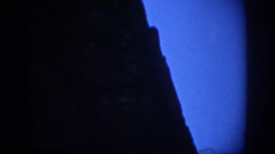 Colorado home-movie frame with a steep rock profile in heavy shadow and blue night sky at the edge.