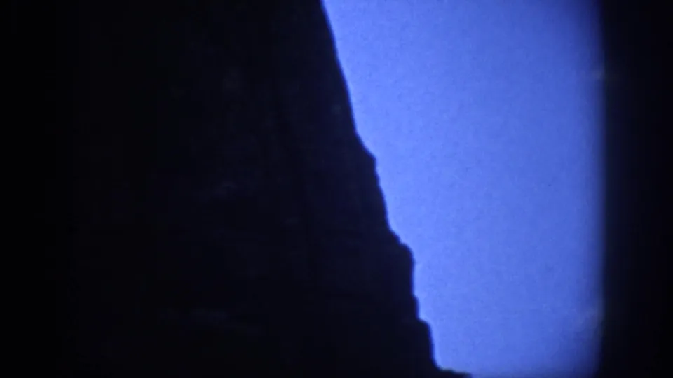 Final Colorado 8mm frame showing a tall, shadowed rock profile beside deep blue twilight sky.