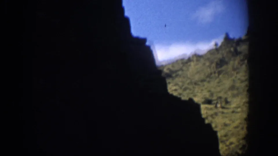 A Colorado canyon view from 1959, with a nearly black rock face dominating the frame and a bright scrub slope beyond.