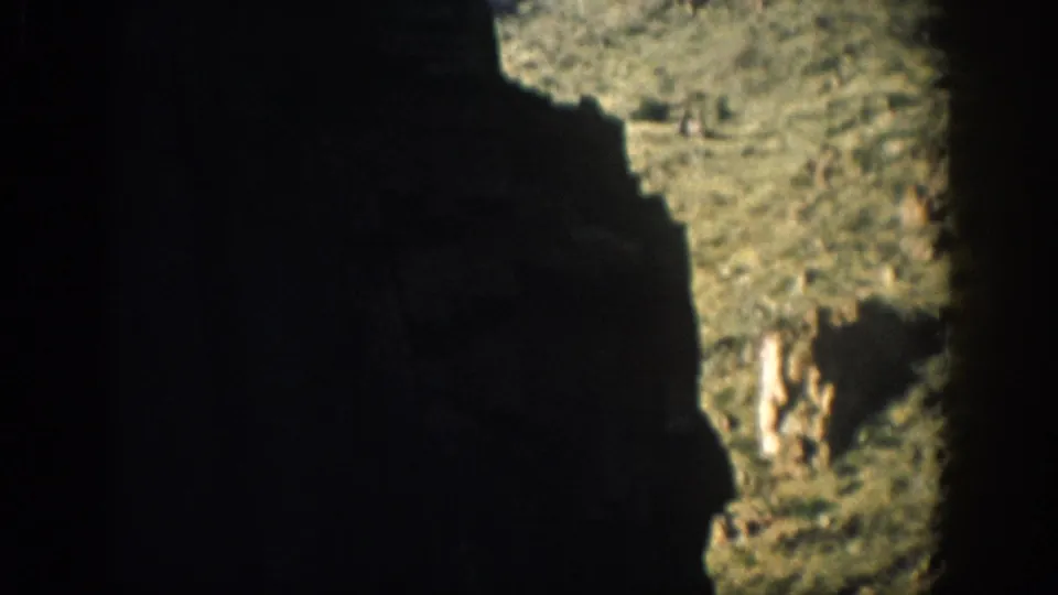 1959 Colorado 8mm frame looking through dark canyon rock toward a sunlit, sparsely vegetated slope.