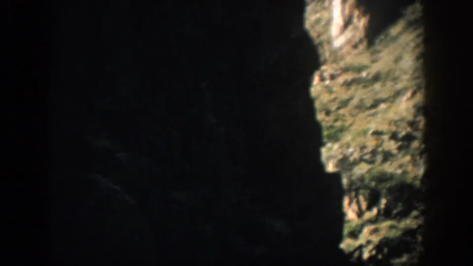 A late-frame 1959 Colorado canyon view showing deep shadow, rough rock texture, and a sunlit slope with sparse vegetation.