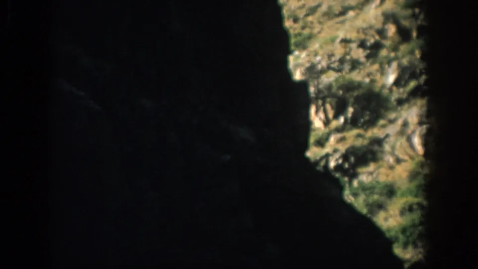 1959 Colorado 8mm frame looking from a dark cave or tunnel toward a sunlit grassy rock opening.