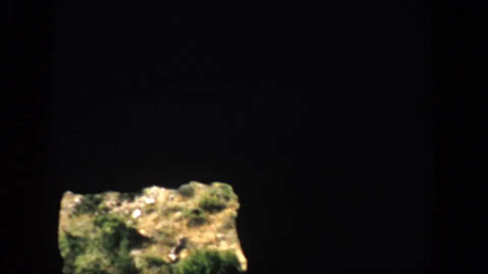 A mostly dark 1959 Colorado 8mm frame with a small sunlit grassy rock area outside the opening.