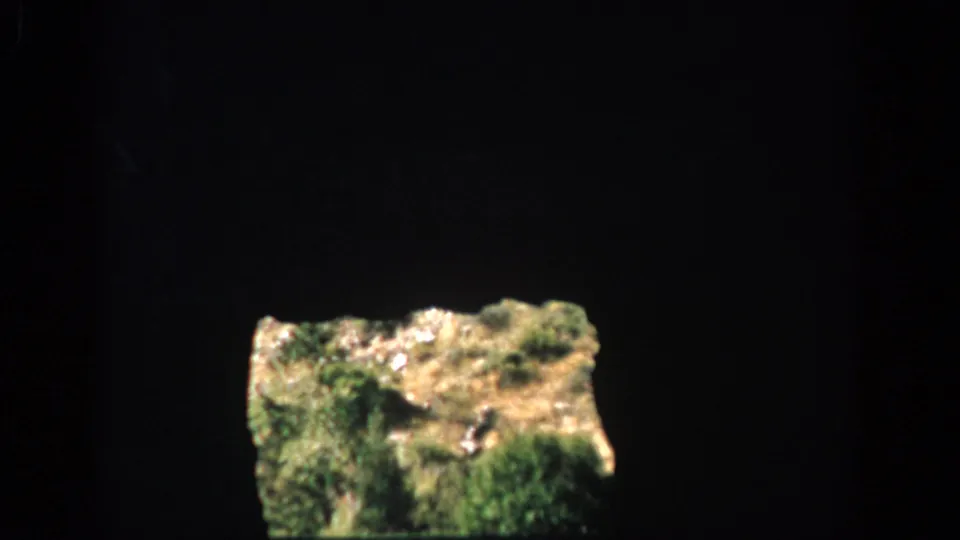 1959 Colorado home-movie frame showing a sunlit grassy rock ledge against a dark cave or tunnel interior.