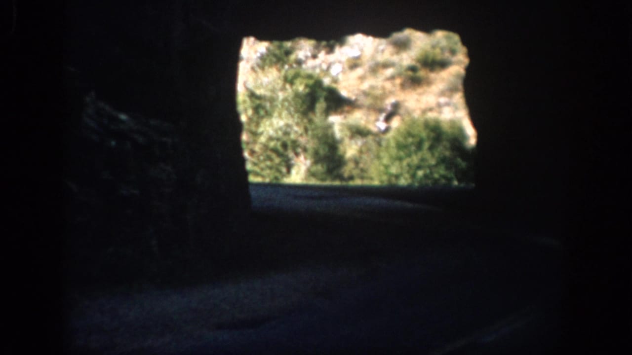 1959 Colorado home-movie frame from inside a dark road tunnel, looking toward a sunlit hillside and vegetation at the exit.