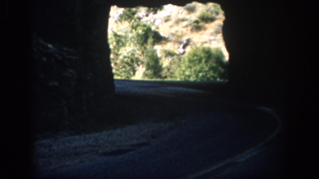 Tunnel road bends toward a bright opening with rocky greenery outside.