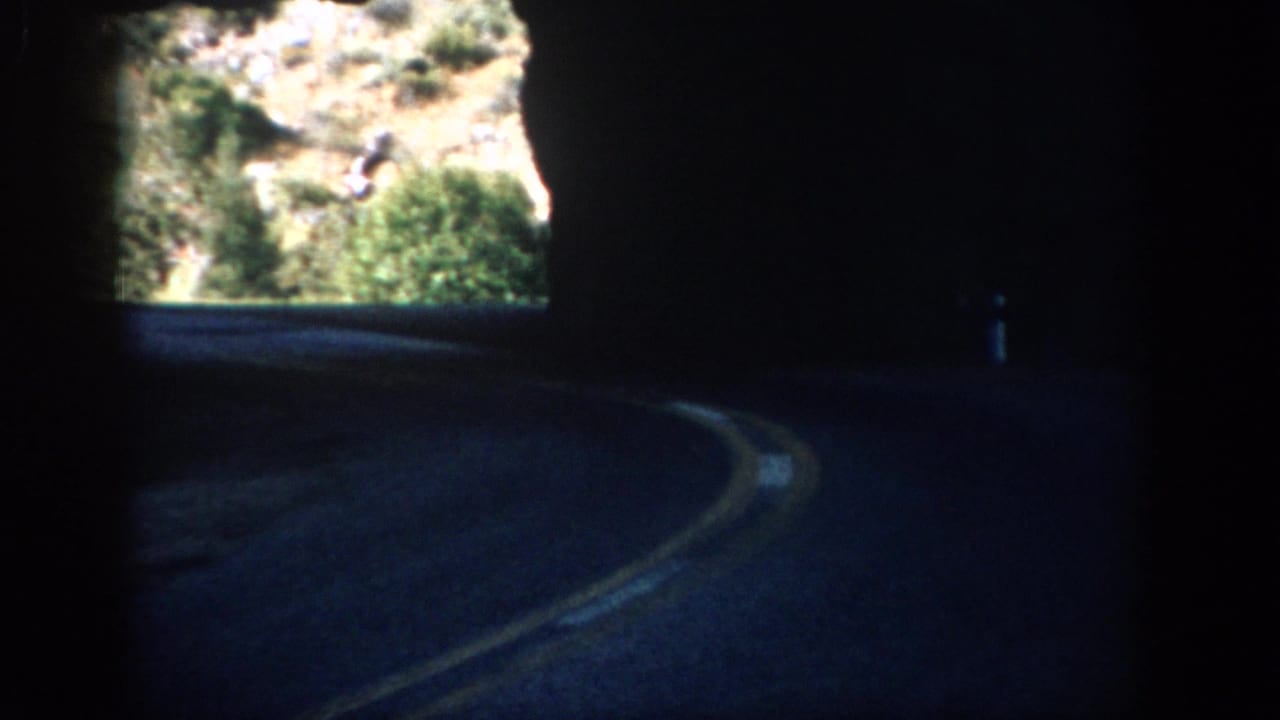 1959 Colorado 8mm frame showing a shadowed tunnel road curving toward a bright rocky mountain opening.