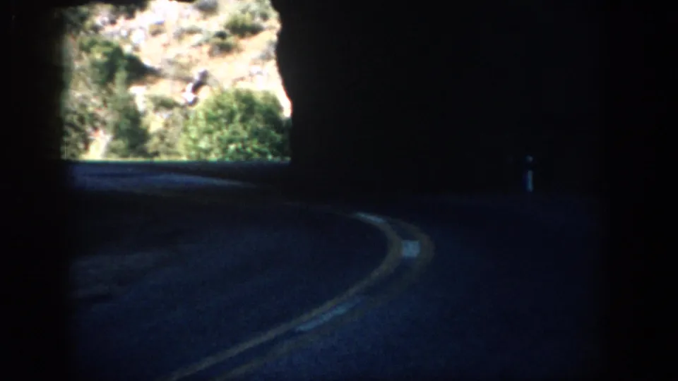 1959 Colorado 8mm frame showing a shadowed tunnel road curving toward a bright rocky mountain opening.