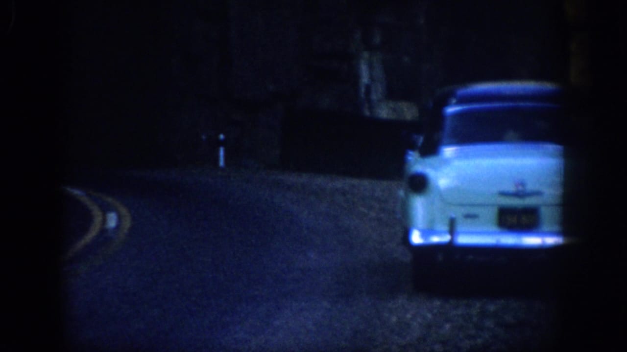 Light blue 1950s sedan at the right edge inside a dark tunnel on a mountain road.