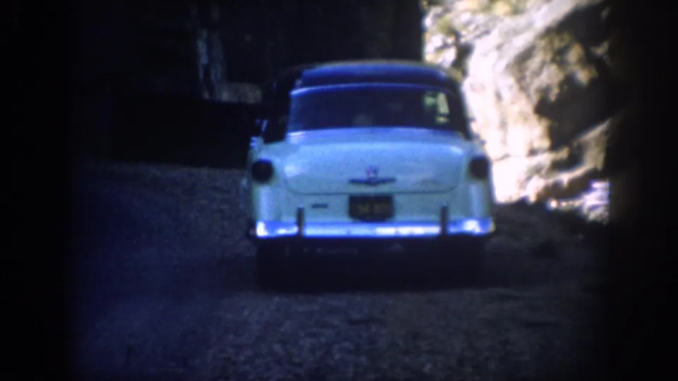 Rear view of a light blue 1950s sedan emerging from a dark Colorado tunnel toward sunlit rock walls.
