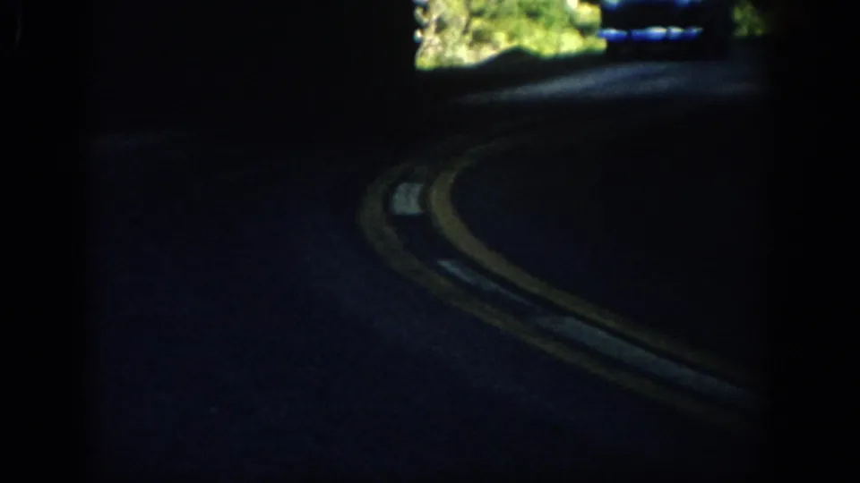 Interior-framed view of a rural Colorado road curve, with yellow centerlines visible in dark 8mm exposure.