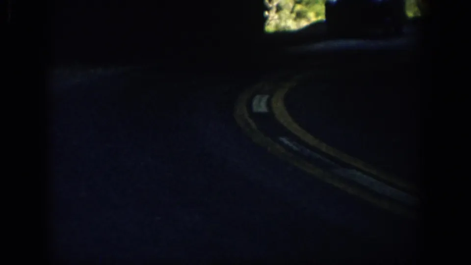 Late-1950s 8mm view from inside a car as a rural Colorado road curves past bright foliage.