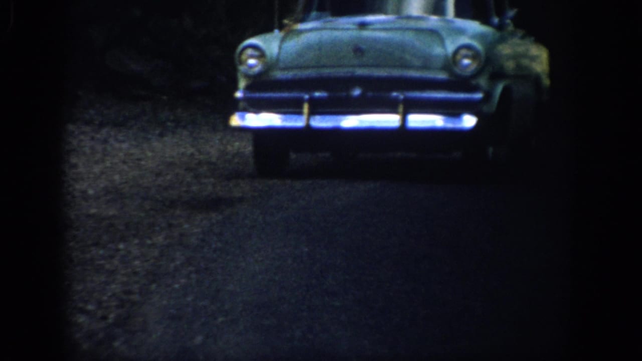 A mid-century car appears on a shadowed Colorado forest road in 1959 home-movie footage.