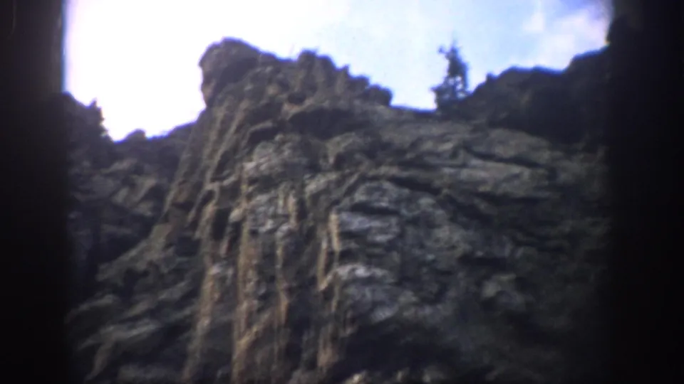 A rugged Colorado cliff face rises under bright sky in a 1959 8mm travel shot.