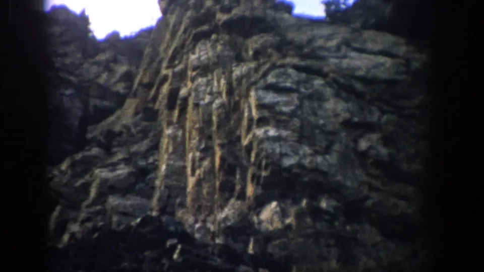 Textured Colorado rock face with vertical mineral streaks fills the frame in soft 8mm color.