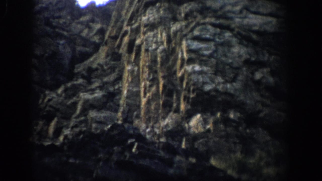 1959 Colorado 8mm frame showing a shadowed rock face with eroded ledges, vertical streaks, and dark viewfinder edges.