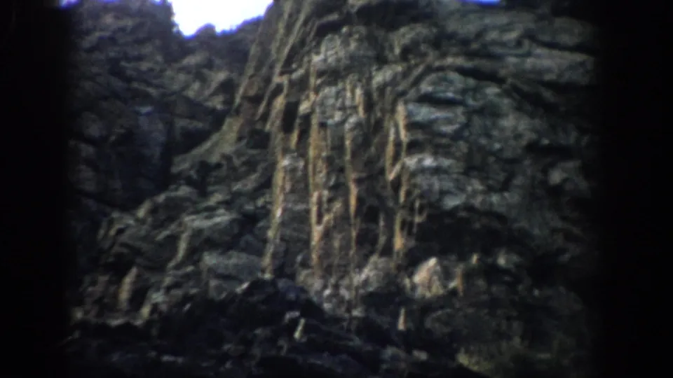 1959 Colorado 8mm frame of a rugged hillside rock formation with striated stone, erosion marks, and muted color.
