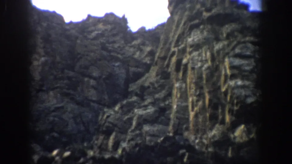 1959 Colorado 8mm frame showing a closer section of hillside stone, with rough layers, vertical streaking, and heavy grain.
