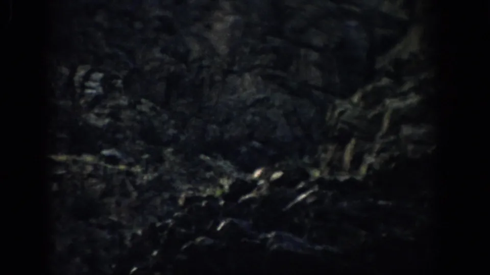 1959 Colorado 8mm frame showing shadowed rocky terrain and part of a streaked formation at the edge of the frame.