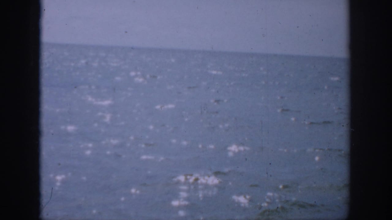 1959 Florida 8mm frame showing a hazy ocean horizon with sunlight on water and dark vertical framing at the sides.