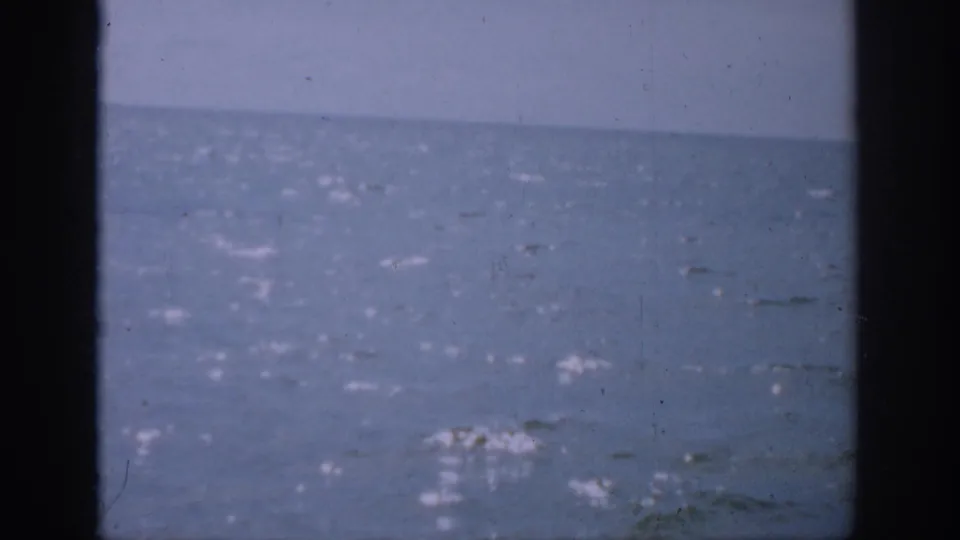 1959 Florida 8mm frame showing a hazy ocean horizon with sunlight on water and dark vertical framing at the sides.