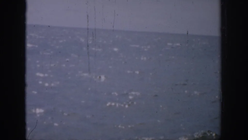 1959 Florida 8mm still with a soft blue ocean, faint sky, sun flecks on the water, and visible vertical film wear.