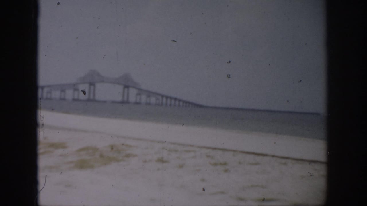 1959 Florida beach view with a long bridge crossing the water in the distance, filmed from a sandy shoreline.