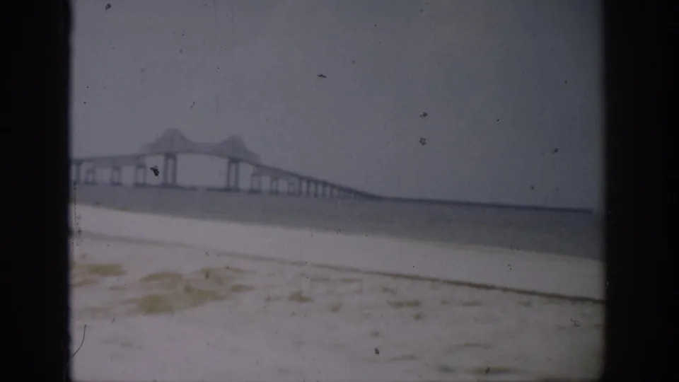 1959 Florida beach view with a long bridge crossing the water in the distance, filmed from a sandy shoreline.