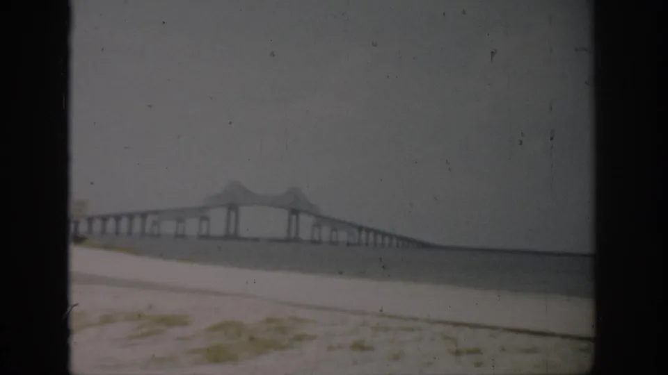 Faded 8mm view of a Florida bridge crossing water, with a pale beach foreground and soft gray sky.