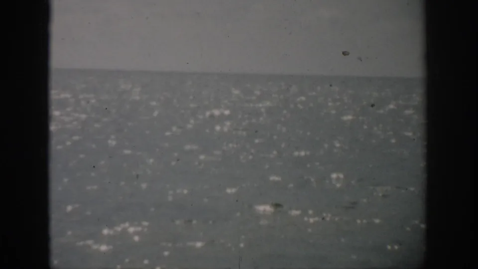 1959 Florida 8mm frame showing bright flecks on the water surface below a gray horizon, with dark borders and minor film wear.