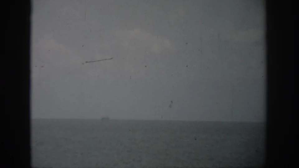 1959 Florida 8mm frame showing a hazy sea horizon, muted sky, and a small boat far in the distance.