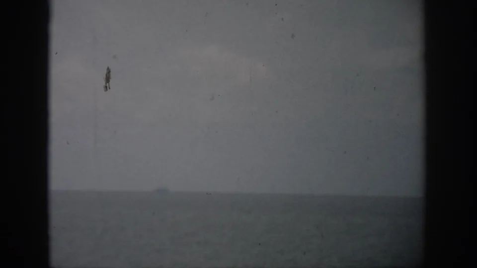 1959 Florida coastal view with a faint boat on the horizon, muted sky, and visible 8mm film texture.