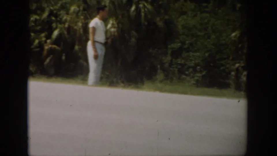 1959 Florida home-movie frame of a man beside roadside vegetation, with the paved road filling the foreground.