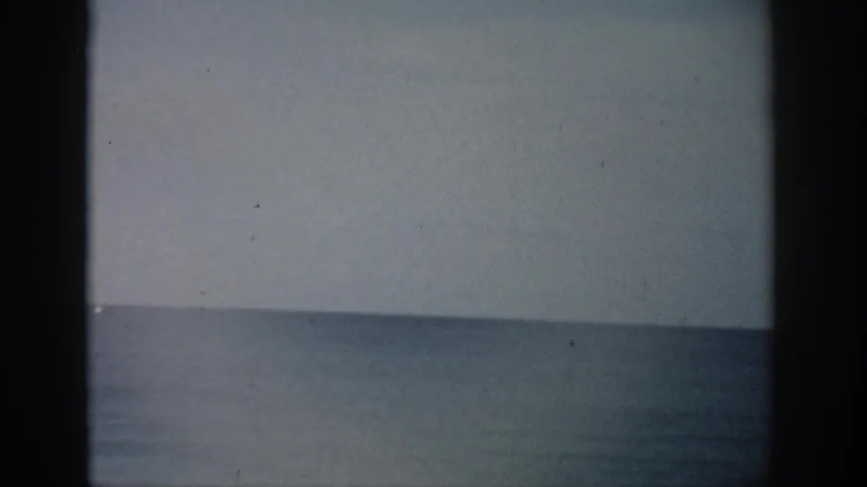 1959 Florida 8mm frame showing a calm ocean horizon under a pale sky, with faded color, grain, and dark film borders.