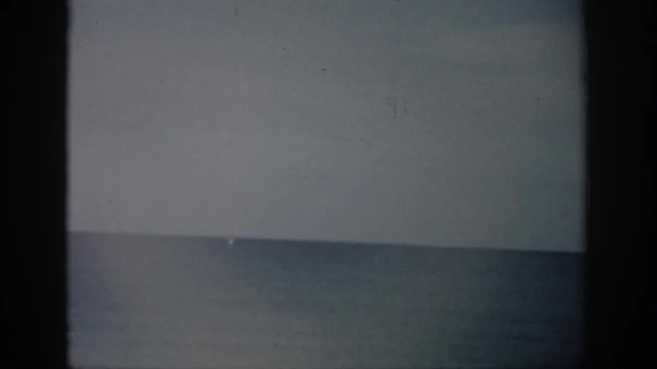 1959 Florida home-movie frame of a muted ocean horizon, with soft exposure, grain, scratches, and dark film edges.