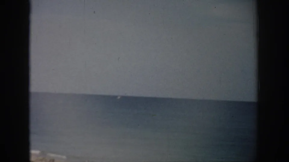 1959 Florida 8mm frame showing calm sea, pale sky, faint surf at the bottom edge, grain, and dark film borders.