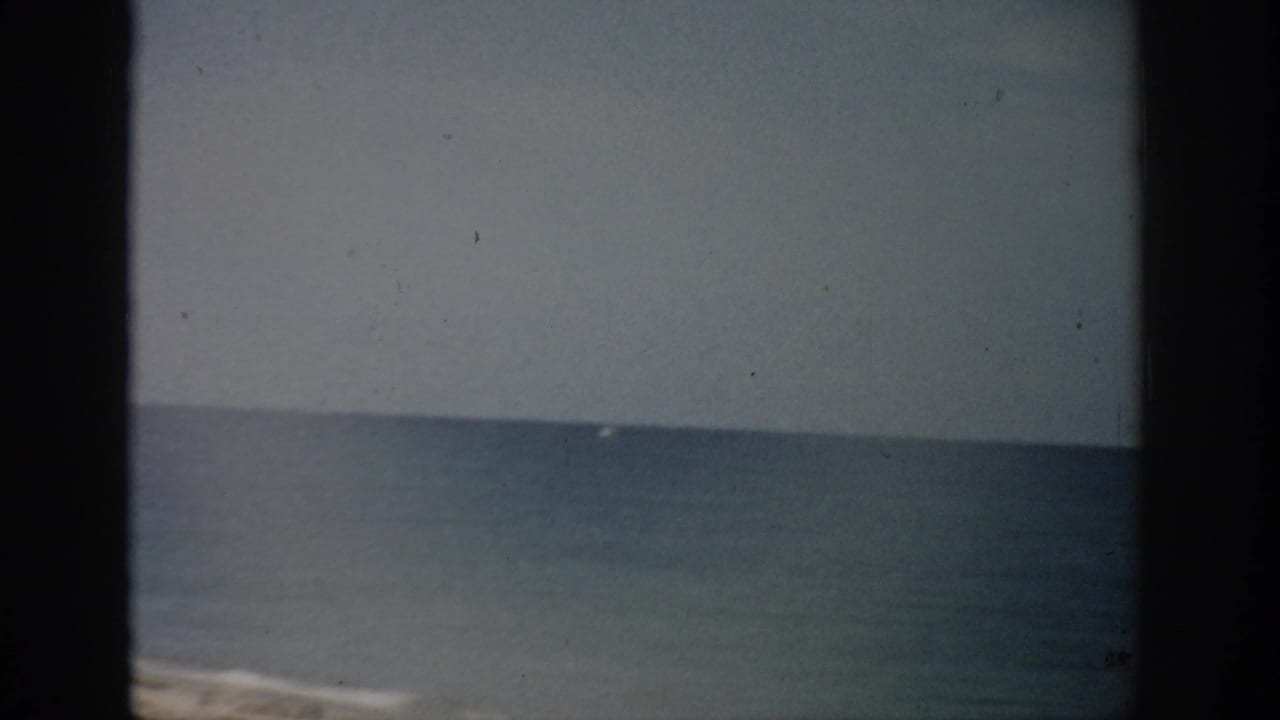 1959 Florida 8mm frame showing a calm blue ocean horizon and pale sandy beach with visible film borders and dust.