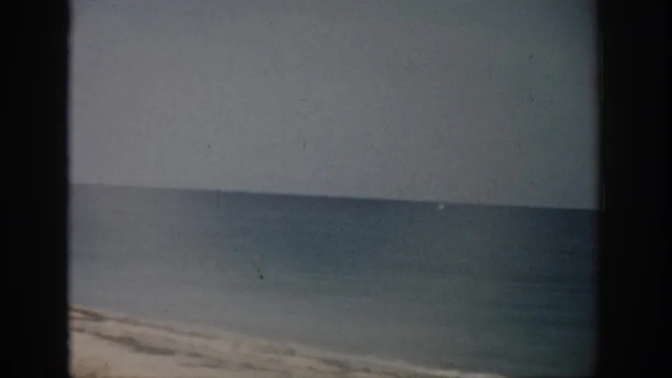 1959 Florida 8mm frame of an empty shoreline, calm water, and level horizon with soft color and visible film artifacts.