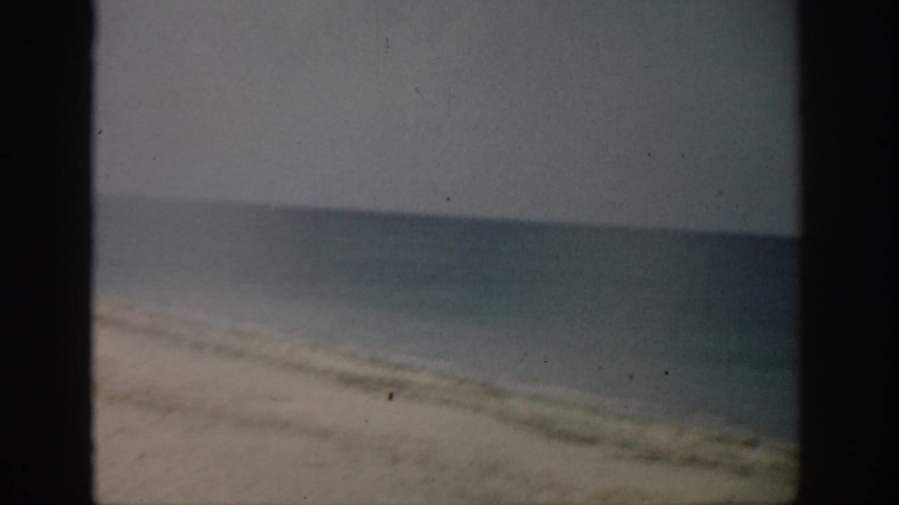 1959 Florida 8mm frame showing a sandy shoreline, calm ocean, pale sky, and dark film borders.