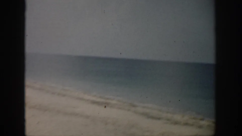 1959 Florida 8mm frame showing a sandy shoreline, calm ocean, pale sky, and dark film borders.