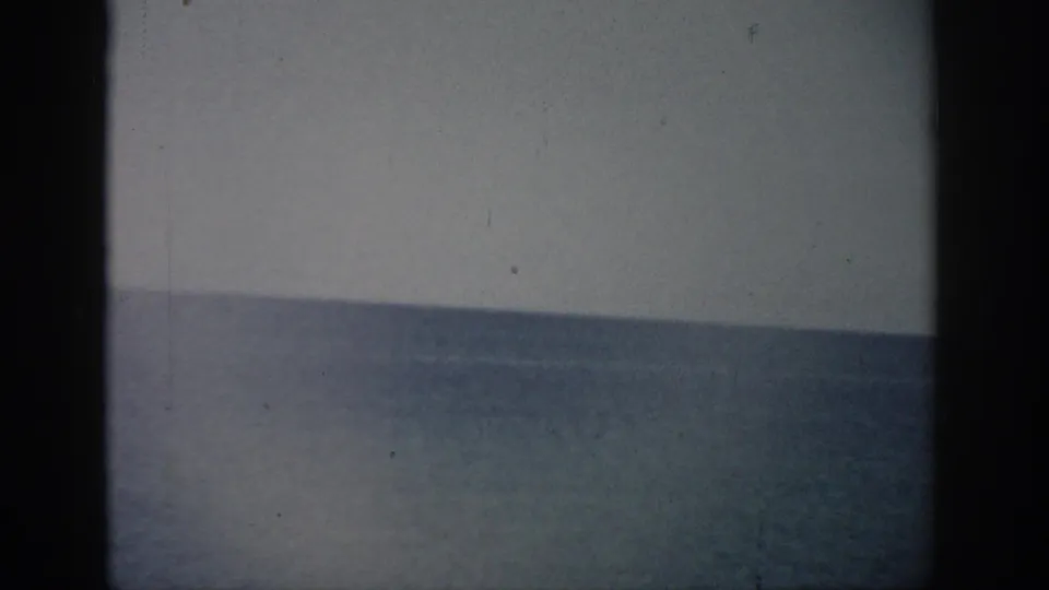 1959 Florida 8mm frame with a calm ocean horizon, muted sky, grain, and visible border shadows.